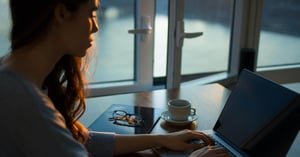 Woman working at laptop computer next to open window