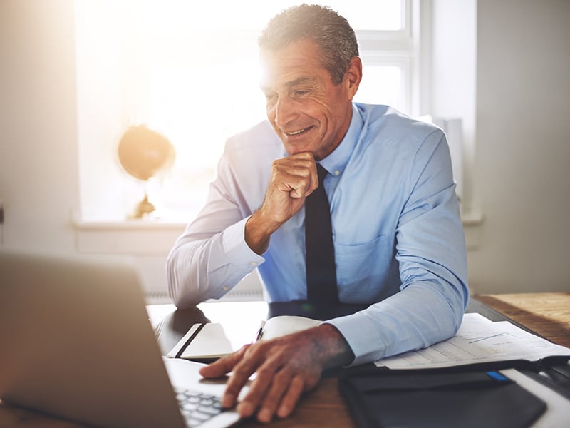 Smiling businessman working on a laptop at his office desk