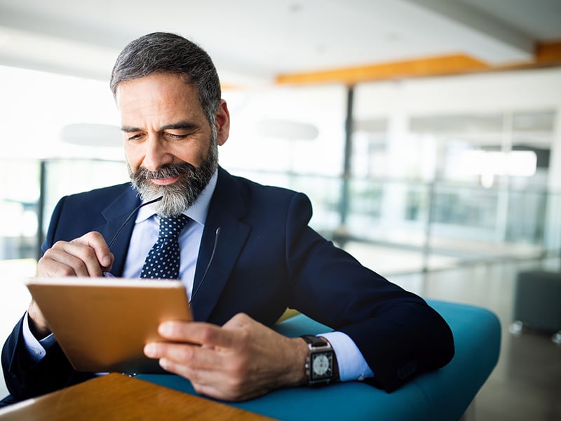 Businessman holding glasses and looking at a tablet