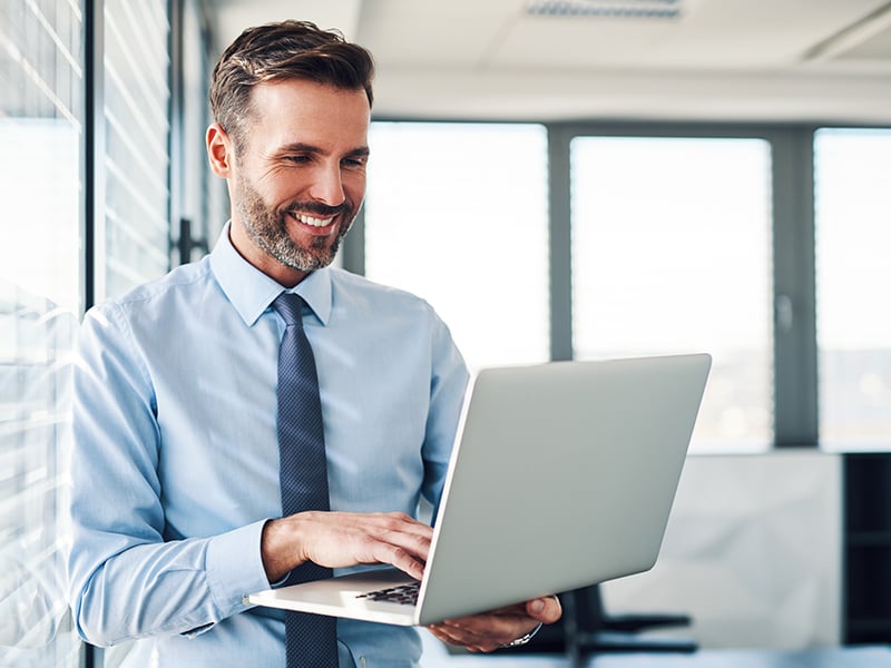 Businessman in modern office looking at a laptop he's holding