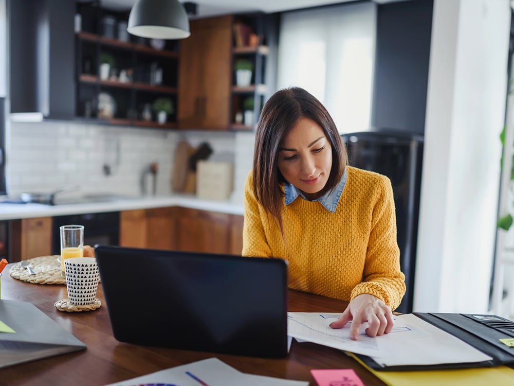 Young businesswoman working at home at a kitchen table while having breakfast