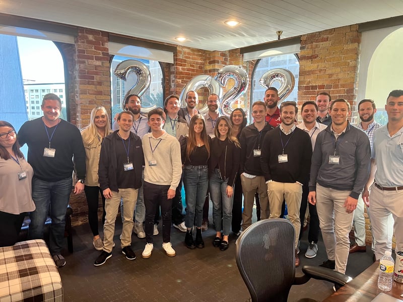 Group of employees posing in an office with balloons spelling out 2022 in the background